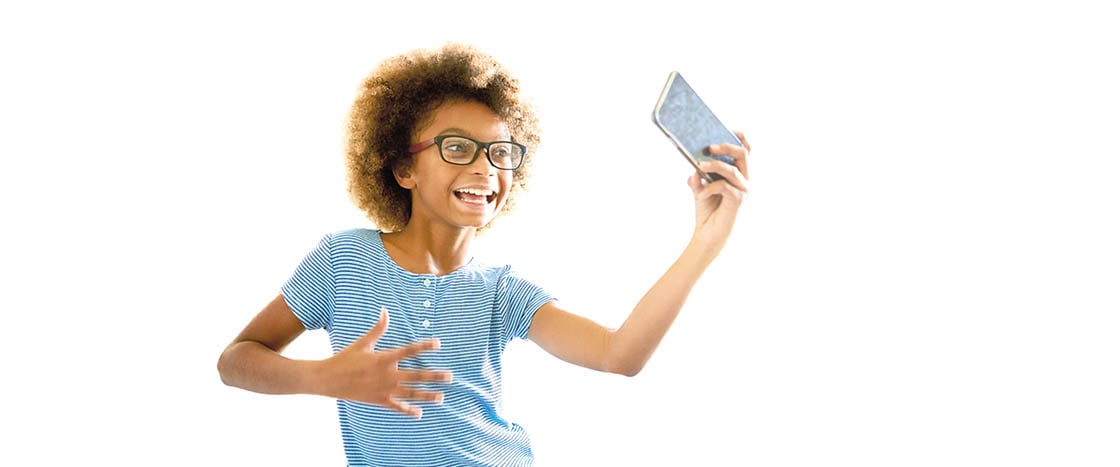 A smiling child holding up a phone to record her dancing