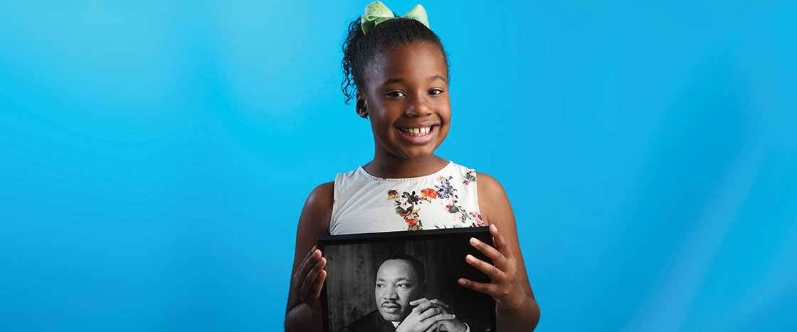 A smiling girl holding a picture of Martin Luther King